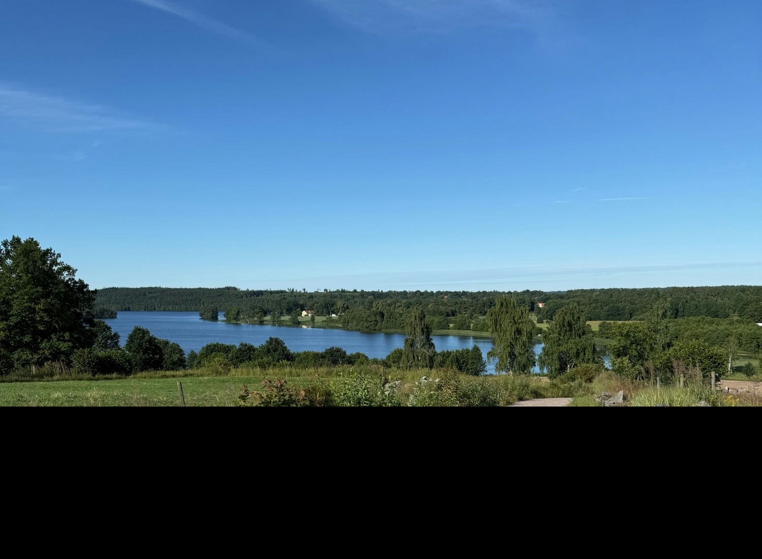 Småländsk landsbygd — en grusväg leder ner mot en sjö omgiven av skog och stenmur.